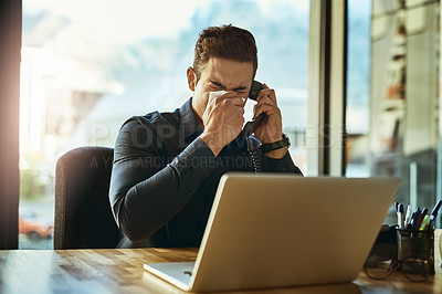 Buy stock photo Shot of a young businessman blowing his nose while speaking on a phone in an office