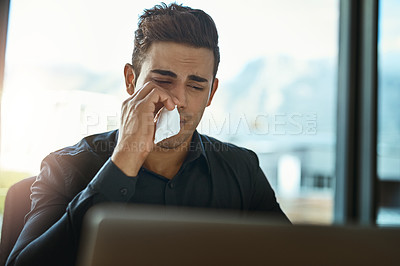 Buy stock photo Shot of a young businessman blowing his nose in an office