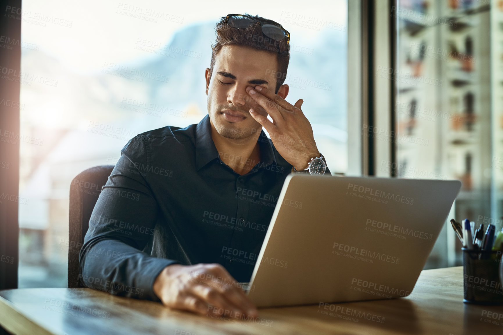 Buy stock photo Shot of a young businessman looking stressed out while working on a laptop in an office