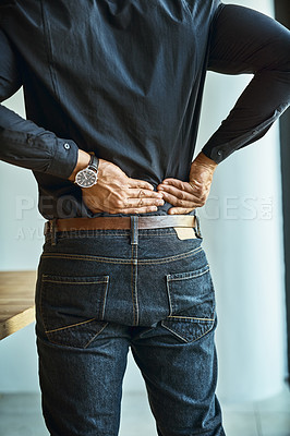 Buy stock photo Shot of a young businessman suffering from back pain while working in an office