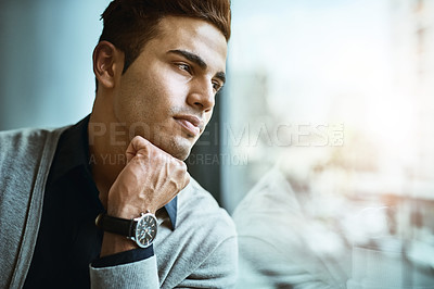 Buy stock photo Shot of a young businessman looking thoughtfully out the window in an office
