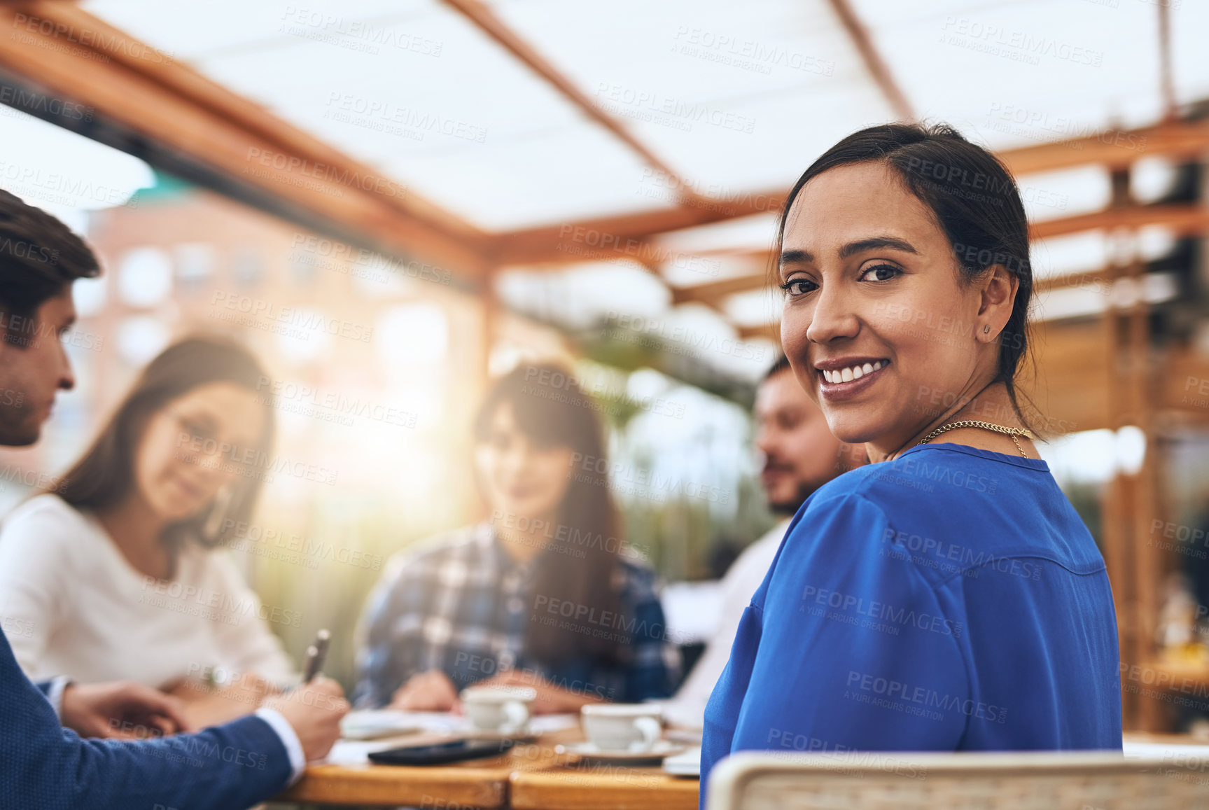 Buy stock photo Portrait of a cheerful young creative businesswoman having a discussion with coworkers at a meeting around a table while looking back at the camera