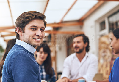Buy stock photo Portrait of a cheerful young creative businessman having a discussion with coworkers at a meeting around a table while looking back at the camera