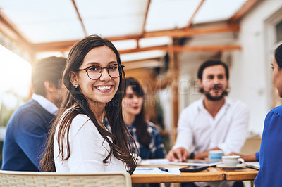 Buy stock photo Portrait of a cheerful young creative businesswoman having a discussion with coworkers at a meeting around a table while looking back at the camera