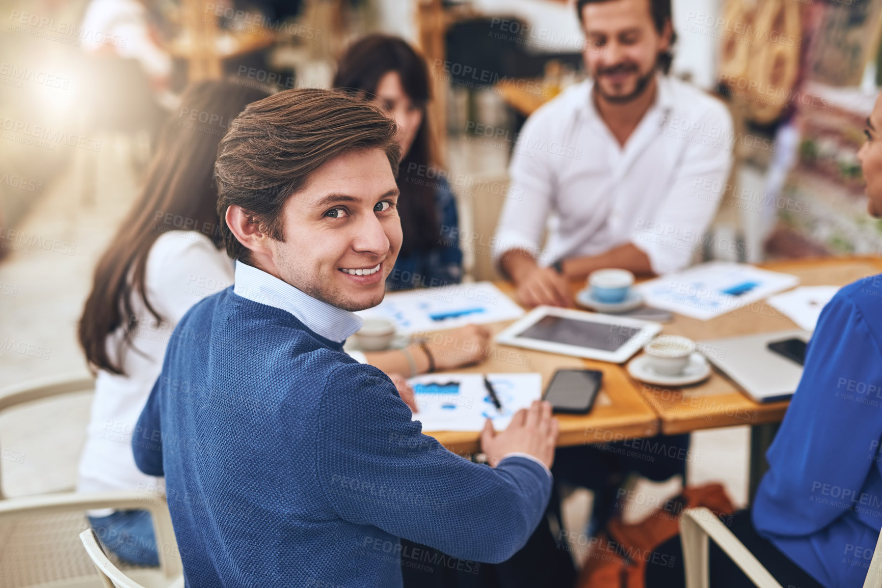 Buy stock photo Portrait of a cheerful young creative businessman having a discussion with coworkers at a meeting around a table while looking back at the camera