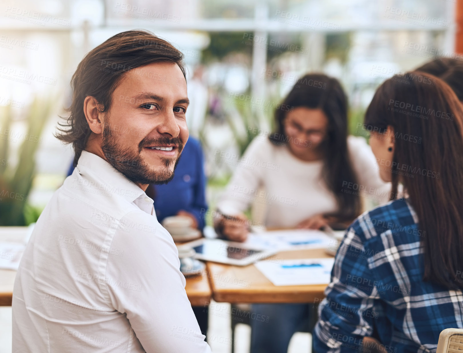 Buy stock photo Portrait of a cheerful young creative businessman having a discussion with coworkers at a meeting around a table while looking back at the camera