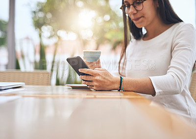 Buy stock photo Shot of a young creative businesswoman using her cellphone while drinking coffee outside a cafe