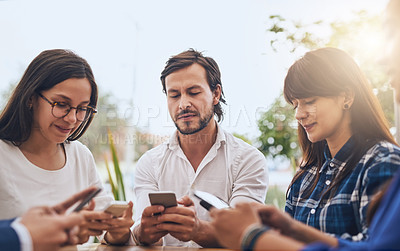 Buy stock photo Shot of a group of young creative businesspeople using their cellphones while standing in a circle outside