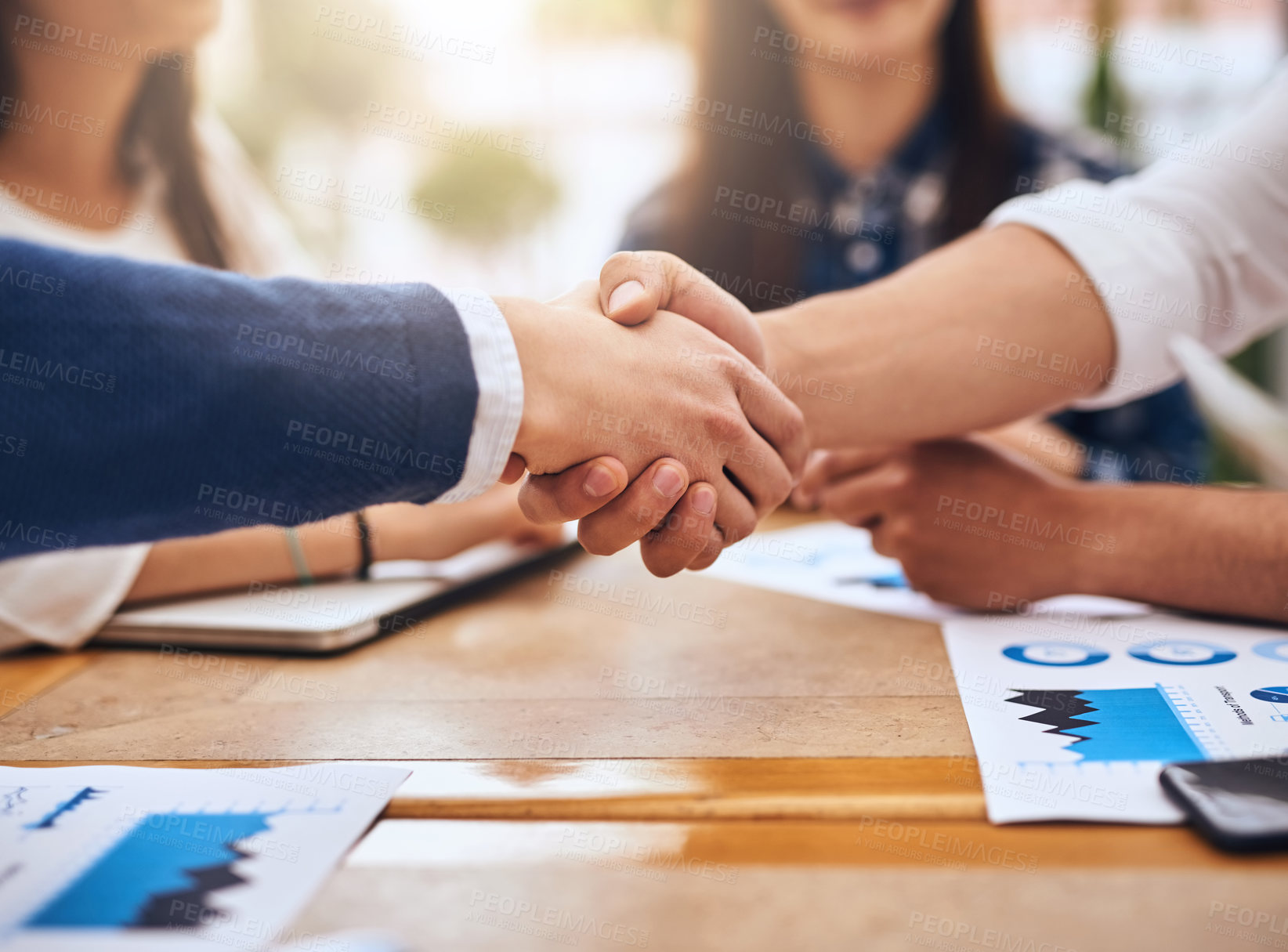 Buy stock photo Shot of two unrecognisable businesspeople shaking hands in agreement over a table at a coffeeshop