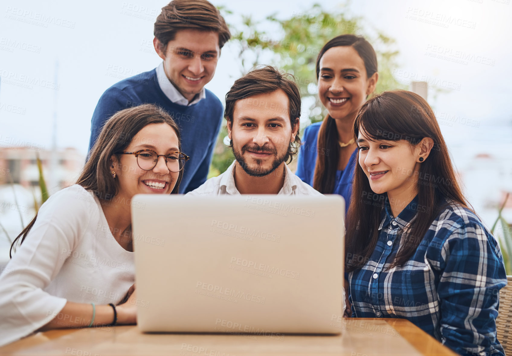 Buy stock photo Shot of a group of young creative businesspeople looking at a laptop screen together outside of a coffeeshop