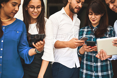 Buy stock photo Shot of a group of young creative businesspeople using mobile devices while talking to each other