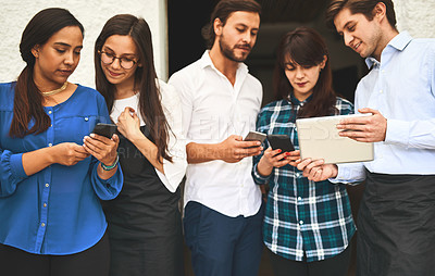 Buy stock photo Shot of a group of young creative businesspeople using mobile devices while talking to each other