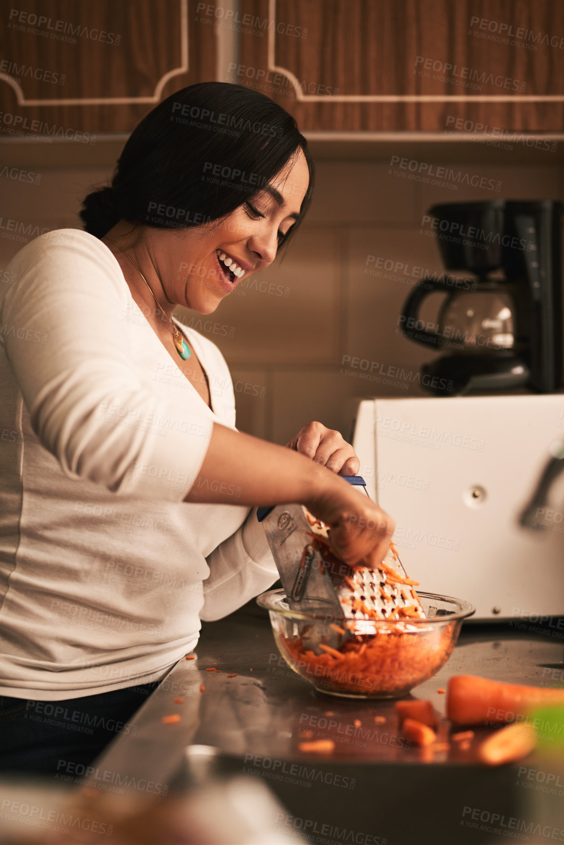 Buy stock photo Shot of a cheerful young woman baking cupcakes and grating carrots inside of a kitchen at home