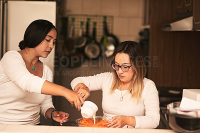 Buy stock photo Shot of two determined young women baking together in a kitchen at home