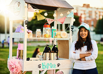 Buy stock photo Shot of a cheerful young woman standing next to her baked goods stall while looking at the camera