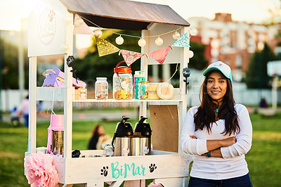 Buy stock photo Shot of a cheerful young woman standing next to her baked goods stall while looking at the camera