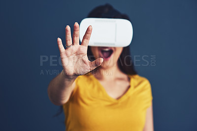 Buy stock photo Studio portrait of an attractive young woman wearing a VR headset against a blue background
