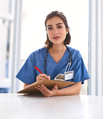 Buy stock photo Portrait of a confident young female doctor making notes on a clipboard while looking at the camera in a clinic