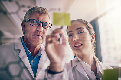 Buy stock photo Shot of two focused scientists working together solving equations on a glass wall in a laboratory