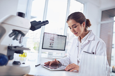 Buy stock photo Shot of a focused young female scientist working on a digital tablet while being seated inside of a laboratory