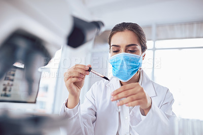 Buy stock photo Shot of a focused young female scientist wearing a surgical mask and doing an experiment while being seated inside a laboratory