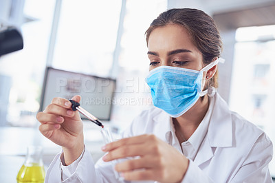 Buy stock photo Shot of a focused young female scientist wearing a surgical mask and doing an experiment while being seated inside a laboratory