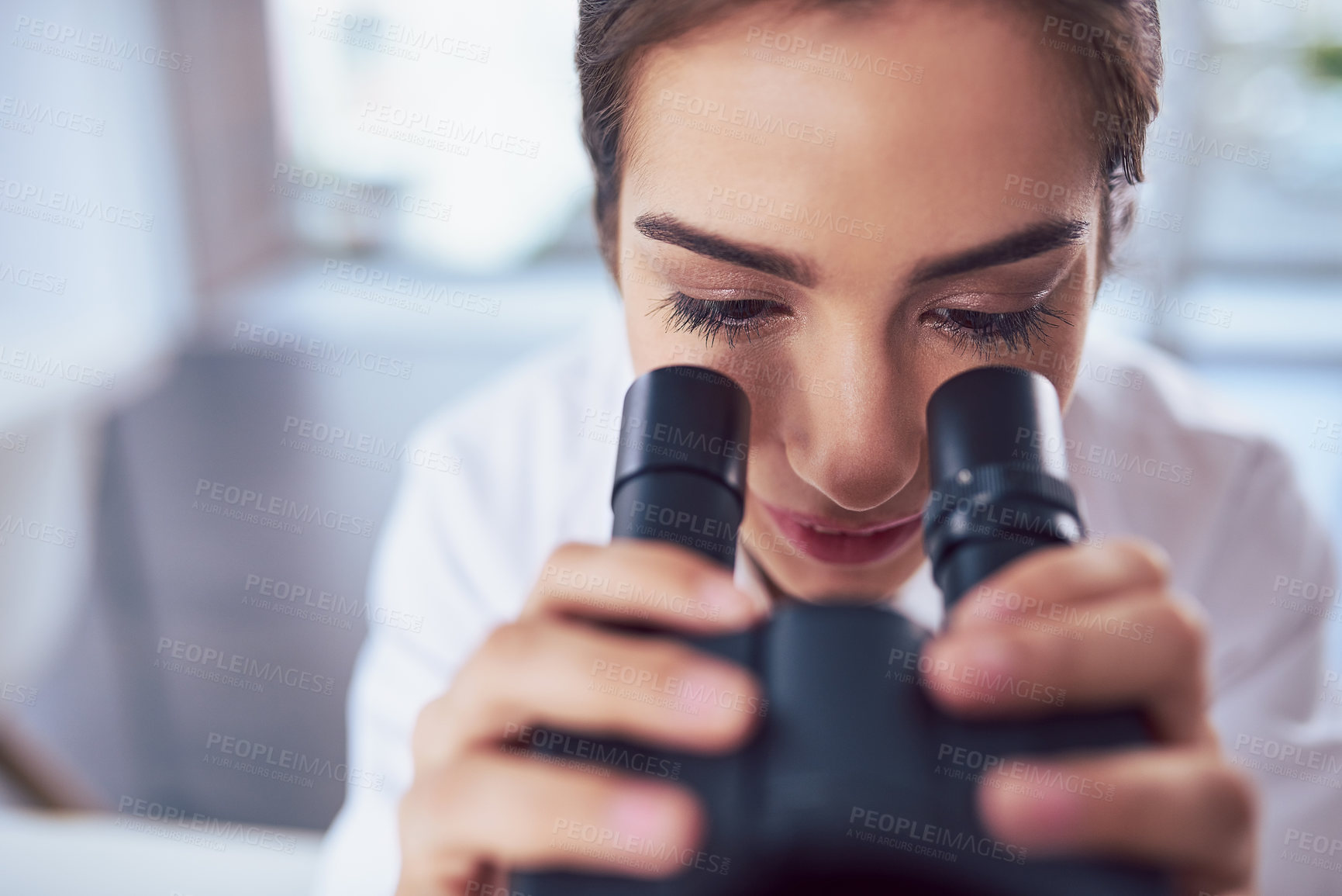 Buy stock photo Closeup of a focused young female scientist looking through the lens of a microscope inside of a laboratory