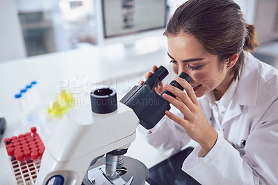 Buy stock photo Shot of a cheerful young female scientist looking through the lens of a microscope while being seated inside of a laboratory