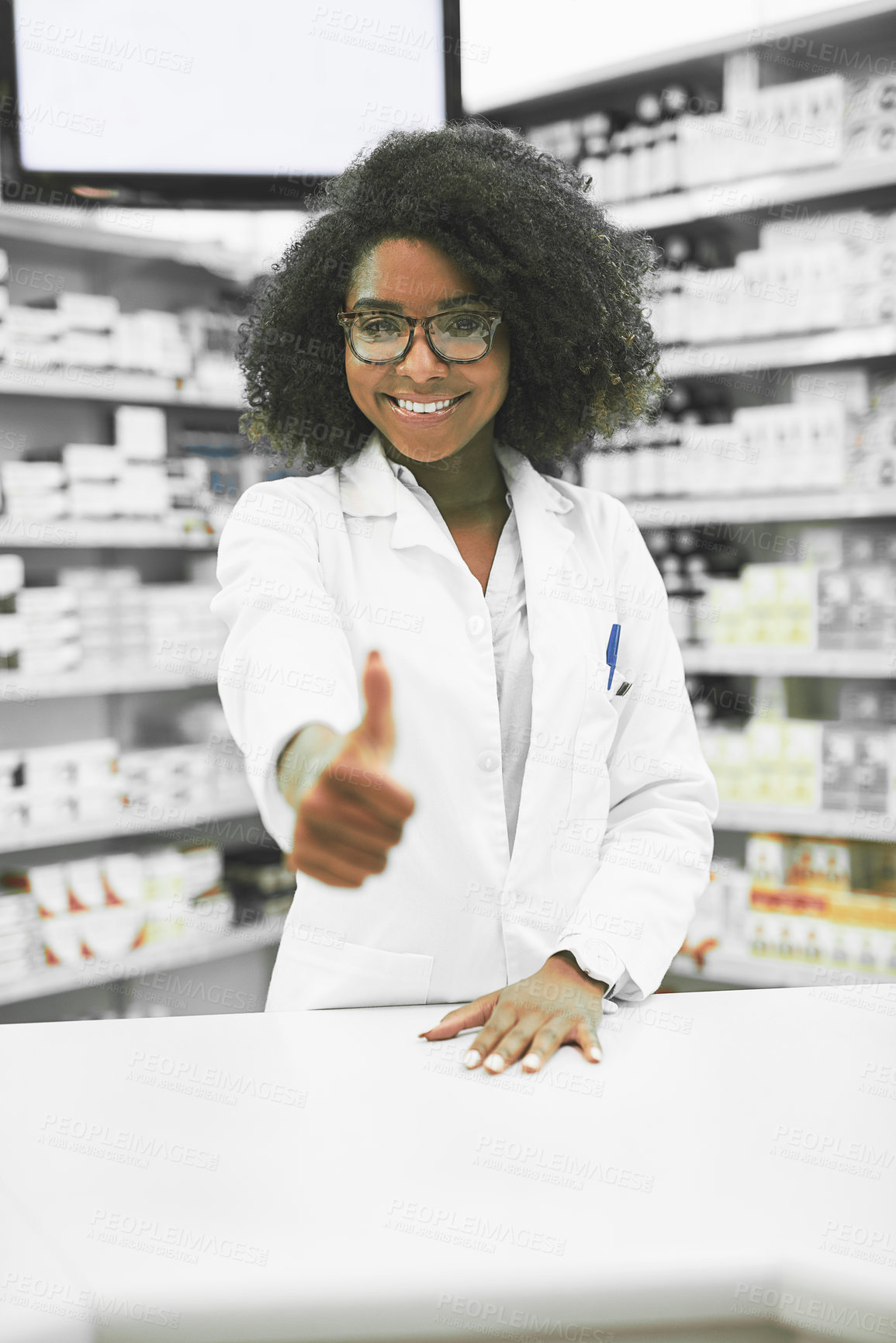 Buy stock photo Portrait of a cheerful young female pharmacist showing thumbs up while looking at the camera in a pharmacy