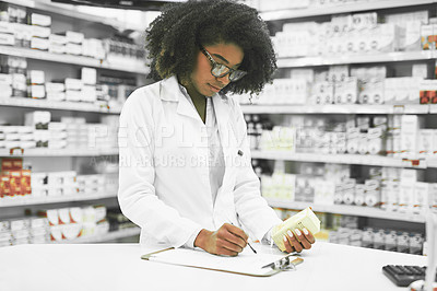 Buy stock photo Shot of a focused young female pharmacist making notes while reading the label of a medication box