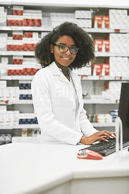 Buy stock photo Portrait of a cheerful young female pharmacist typing on a computer while looking at the camera