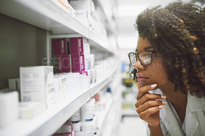 Buy stock photo Shot of a focused young female pharmacist looking closely at medication on a shelf inside a pharmacy