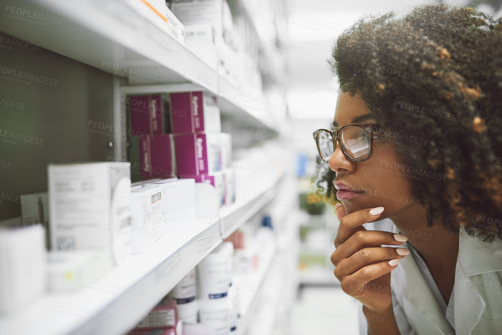 Buy stock photo Shot of a focused young female pharmacist looking closely at medication on a shelf inside a pharmacy