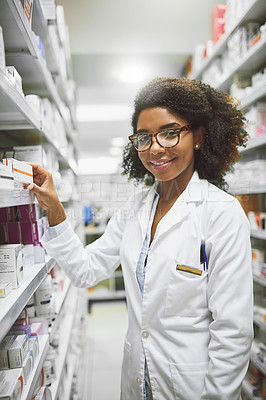Buy stock photo Portrait of a cheerful young female pharmacist putting medication on shelves while looking at the camera in a pharmacy