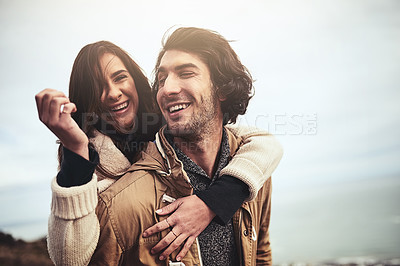 Buy stock photo Portrait of a affectionate young woman having a piggyback ride on her boyfriend's back while looking at the camera outside