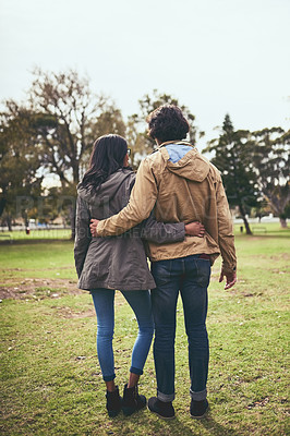 Buy stock photo Rearview shot of a affectionate young unrecognisable couple going for a walk while holding each other outside in a park