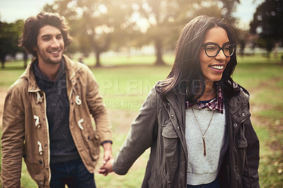 Buy stock photo Shot of a cheerful young couple walking and holding hands together outside in a park