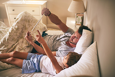 Buy stock photo Shot of a father and his little son using a digital tablet while lying in bed at home