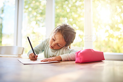 Buy stock photo Shot of a focused little girl drawing pictures in a book while being seated at a table at home