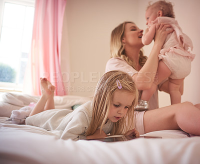 Buy stock photo Shot of a little girl using a digital tablet while bonding with her mother and sister on the bed