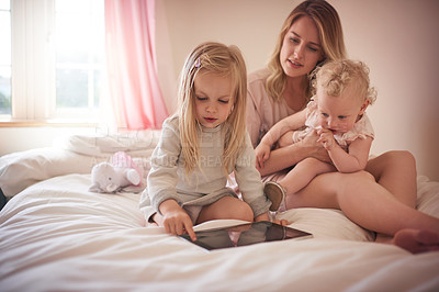 Buy stock photo Shot of a little girl using a digital tablet while bonding with her mother and sister on the bed