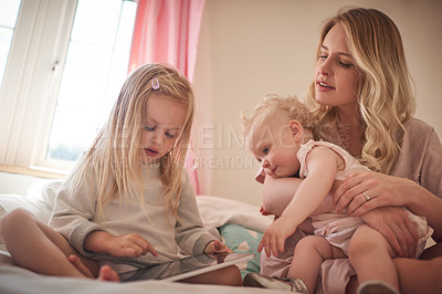 Buy stock photo Shot of a little girl using a digital tablet while bonding with her mother and sister on the bed