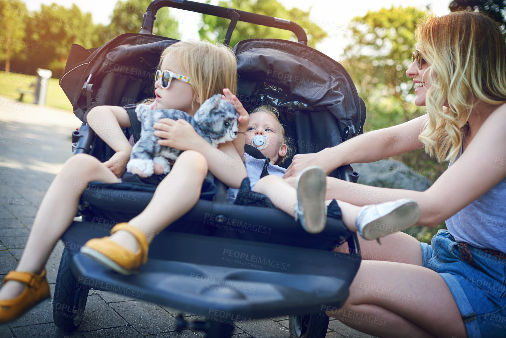 Buy stock photo Shot of a young woman putting her daughters into a pram on a day outdoors