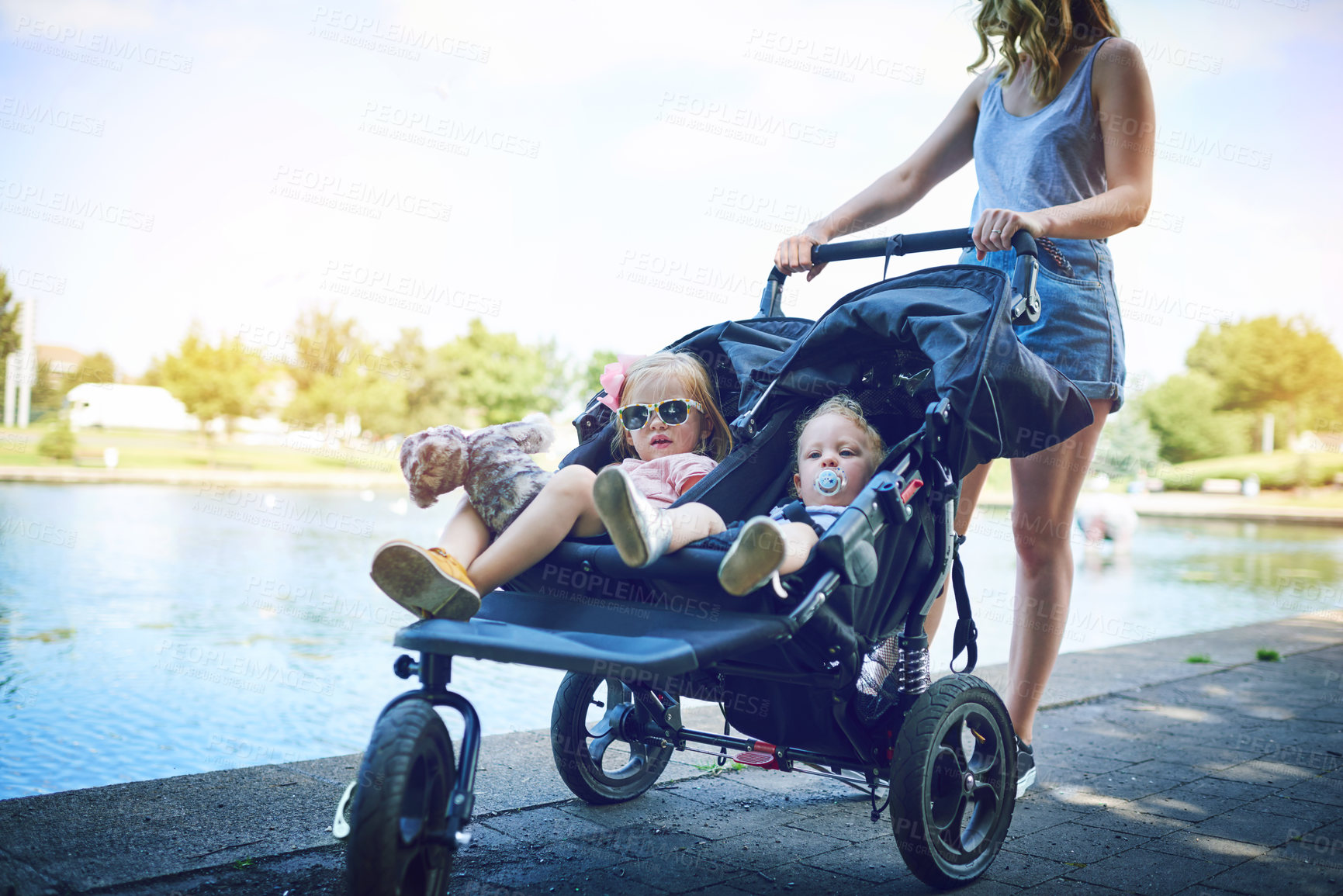 Buy stock photo Shot of a young woman pushing her daughters in a pram on a day outdoors