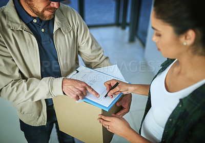 Buy stock photo Shot of a young woman signing for a package from a delivery man