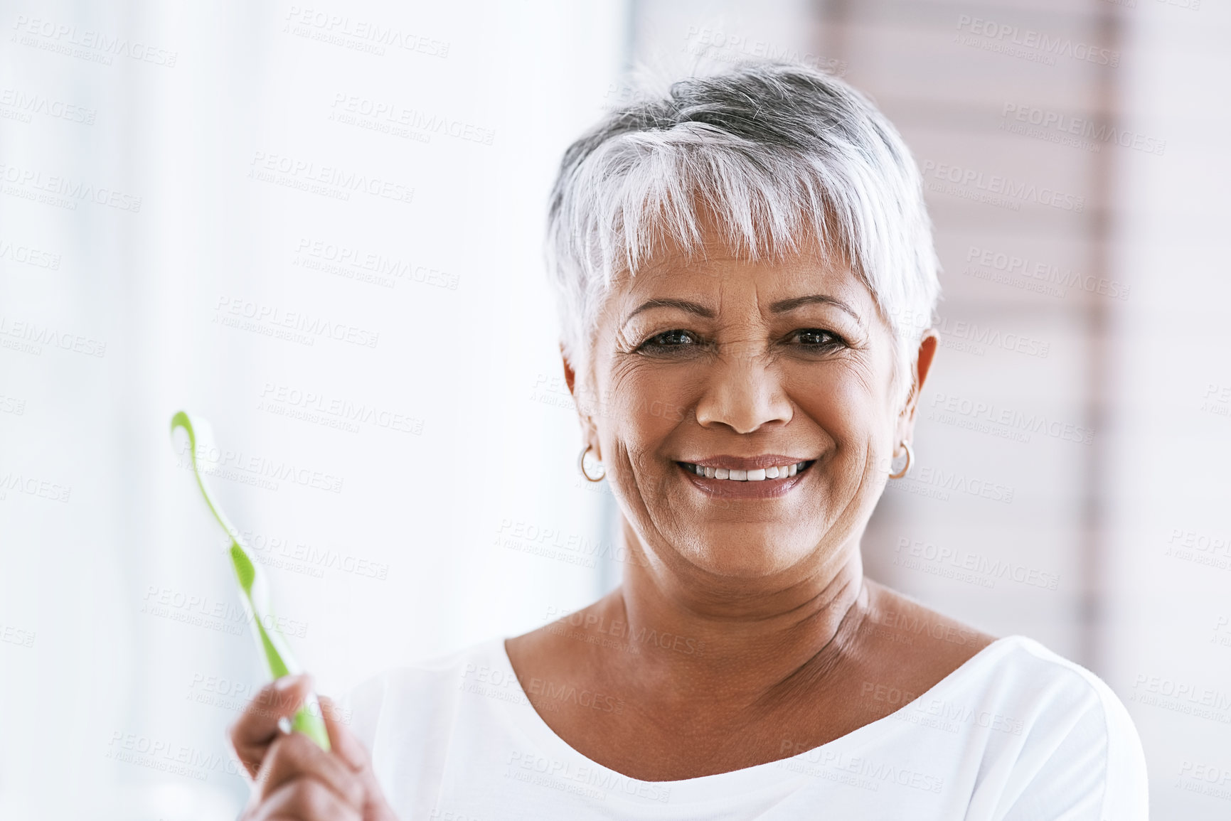 Buy stock photo Portrait of a cheerful mature woman holding a toothbrush while looking into the camera at home