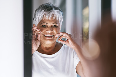 Buy stock photo Portrait of a cheerful mature woman flossing her teeth while looking into a mirror at home