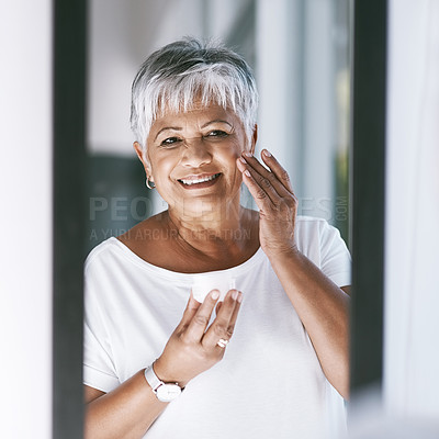 Buy stock photo Shot of a cheerful mature woman applying skin cream on her face while looking into a mirror at home