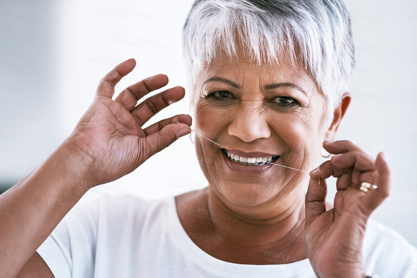 Buy stock photo Portrait of a cheerful mature woman flossing her teeth while looking at the camera at home