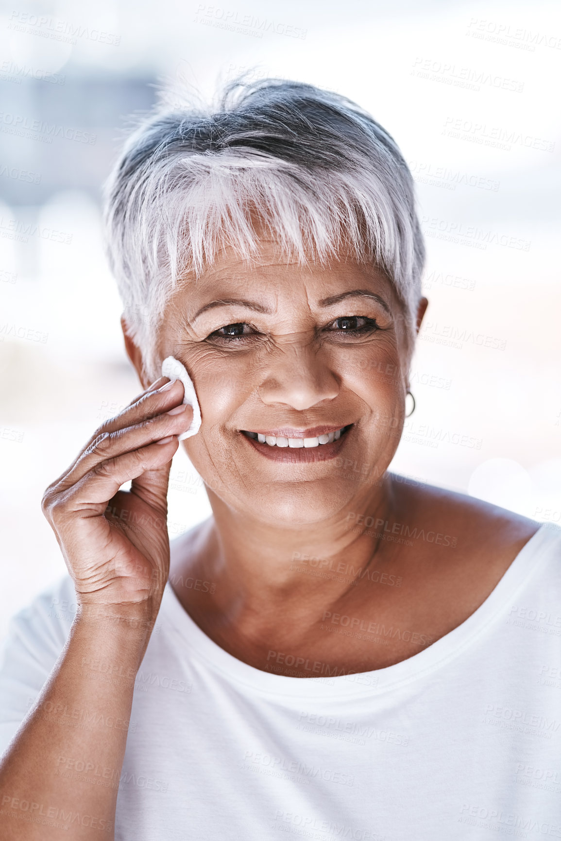 Buy stock photo Portrait of a cheerful mature woman applying makeup remover on her face while looking at the camera